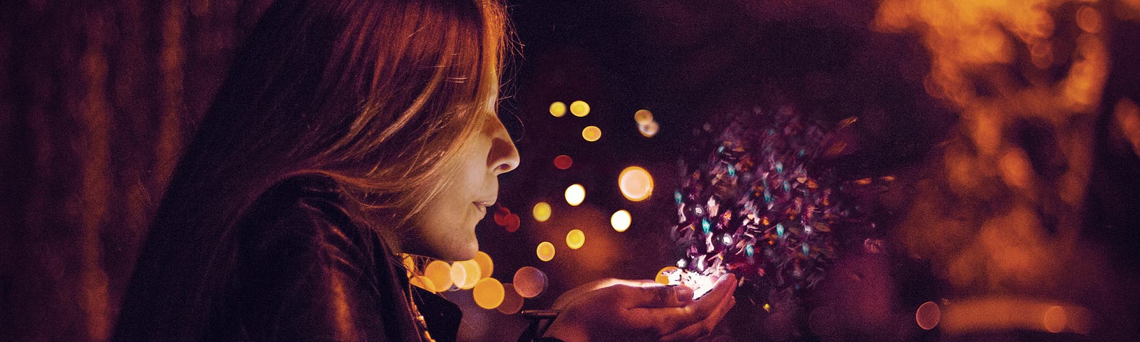 A woman blowing colourful, glowing particles from the palms of her hands into the air.