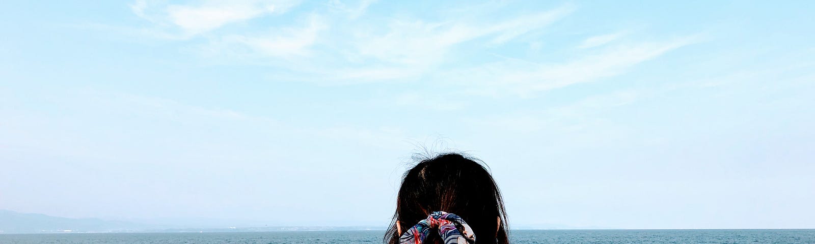 A girl with a pink shirt and blue backpack is taring far into the ocean.