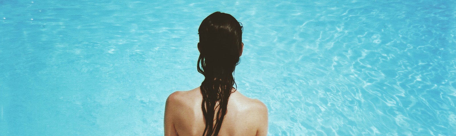 Photo of the back of a female sitting by a pool with wet hair