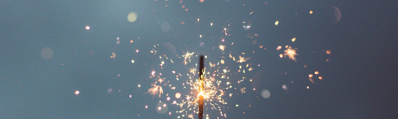 shadow of a hand holding up a sparkler against a dark grey or indigo sky