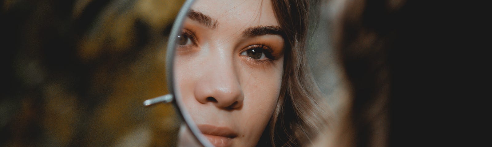 A dark-haired woman looks in a round mirror