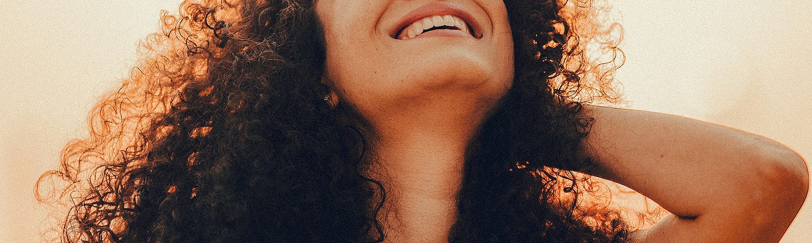 Woman with voluminous curly hair leaning her head back and laughing.