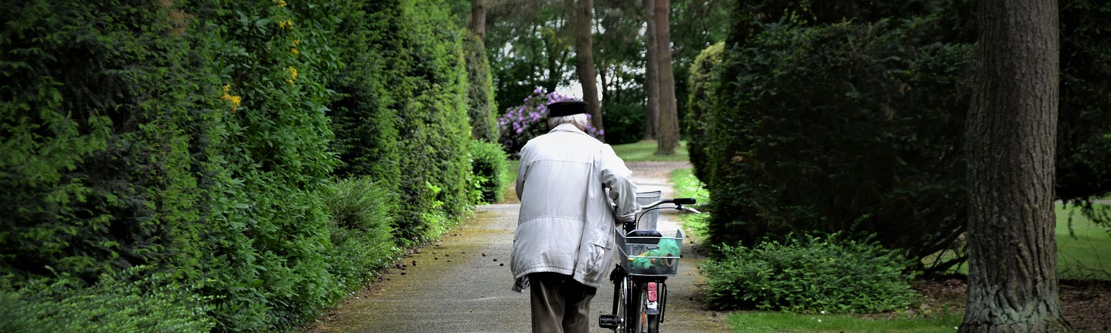 Old man with black cap and white coat on walkway with bicycle