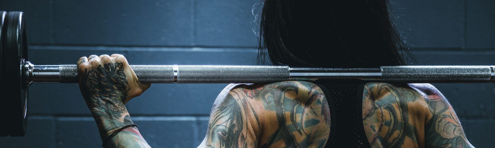 The back of a strong, tattooed woman lifting weights at a gym
