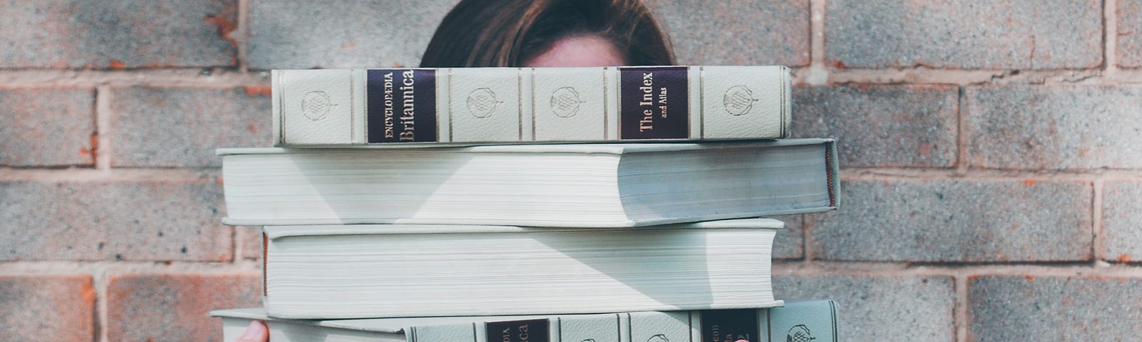 A photo of an individual holding a stack of books in front of their face