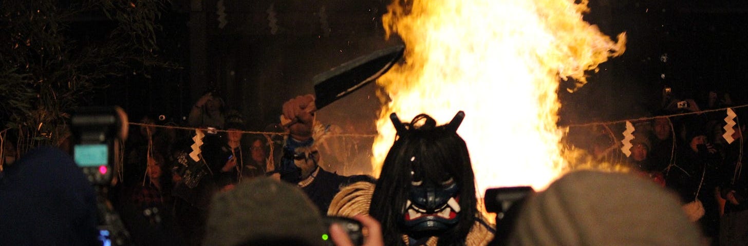 A blue faced demon stands in front of a bonfire while weilding a knife