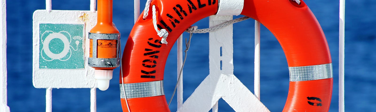 Bright blue background with white fence from which hangs a bright orange life saving device