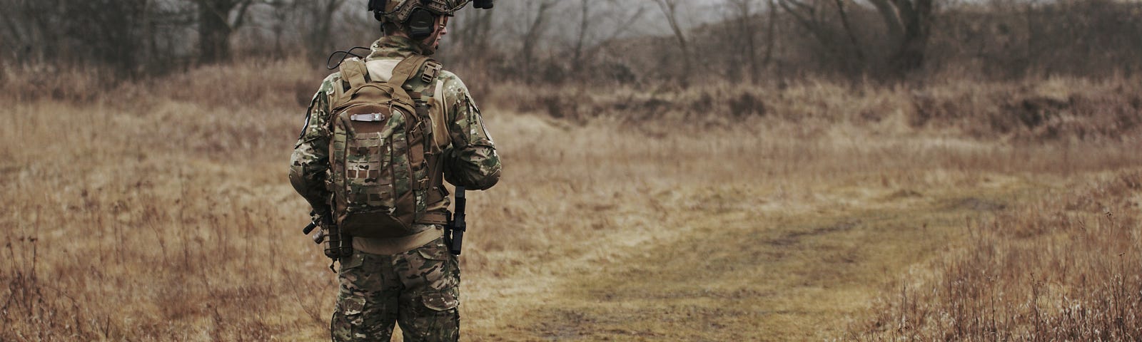 Photo shows a person in a military camo uniform walking on a trail.