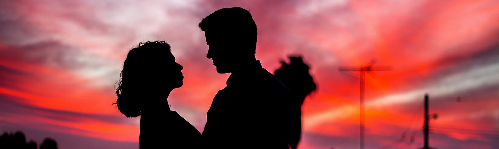 A shadow of a boy and girl looking into each other’s eyes against a purple and red sky backdrop.