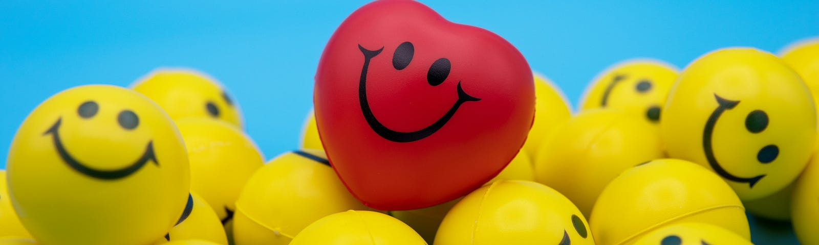 a pile of yellow smiley face balls with one red heart shaped ball on top