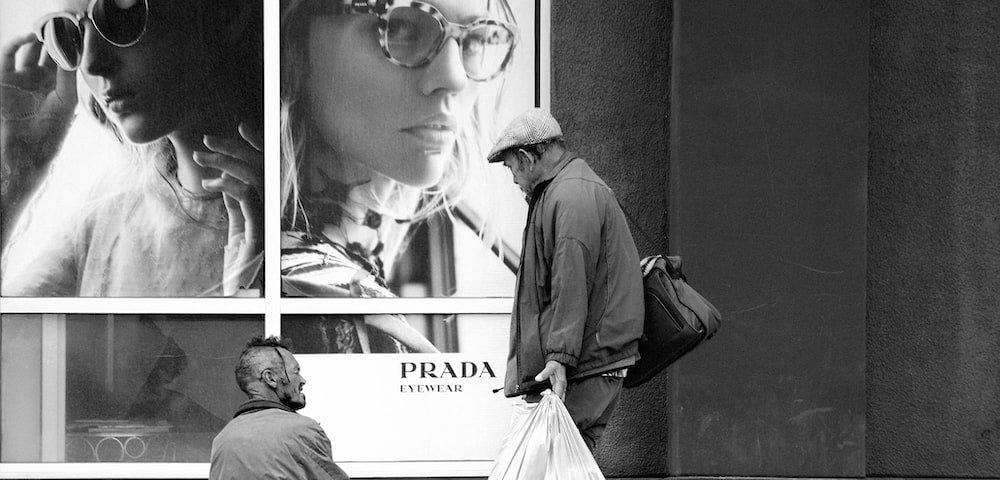 A man looking at a homeless person in front of a luxury store indicating how unequal the society with the rich and poor is