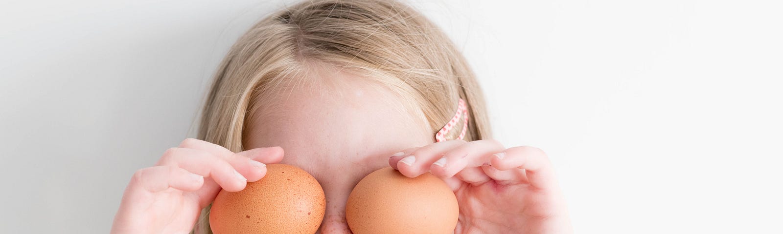 A young girl holding fresh eggs over her eyes — Not unlike my first baking experience!