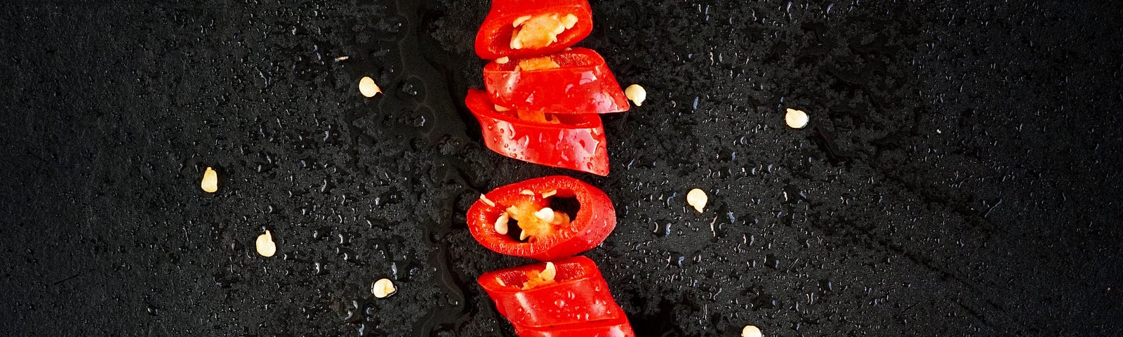 A red pepper, displayed vertically and cut multiple times horizontally.