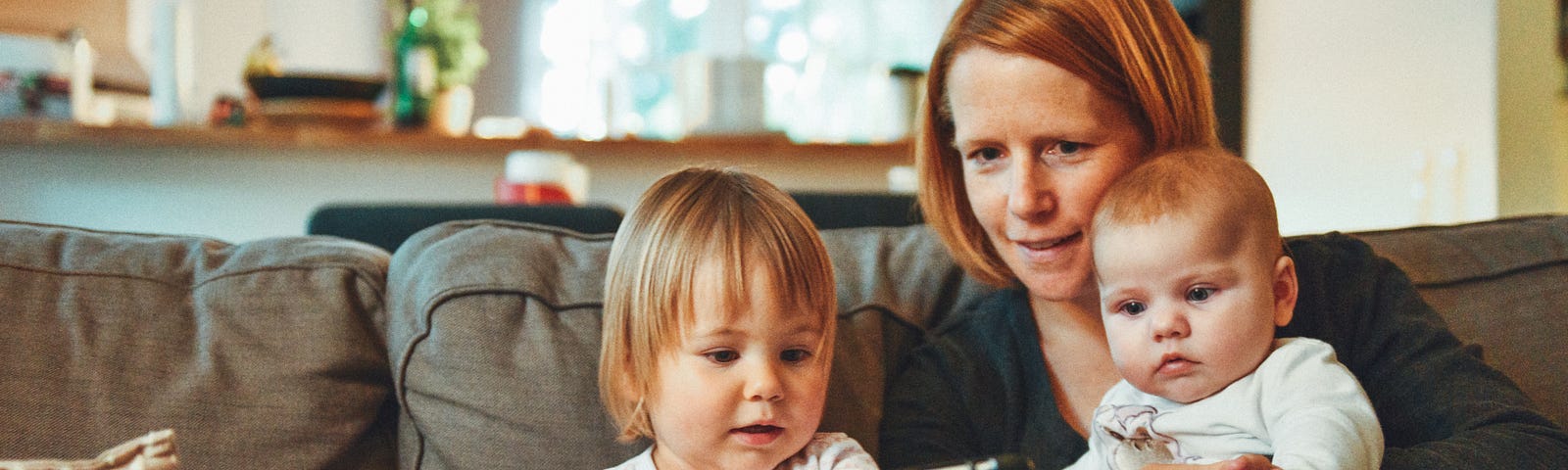 Mom sitting on couch with two little ones looking at tablet