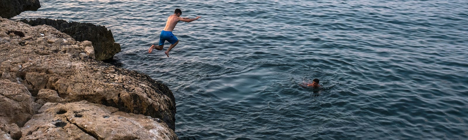 A man jumping off of a cliff into the ocean