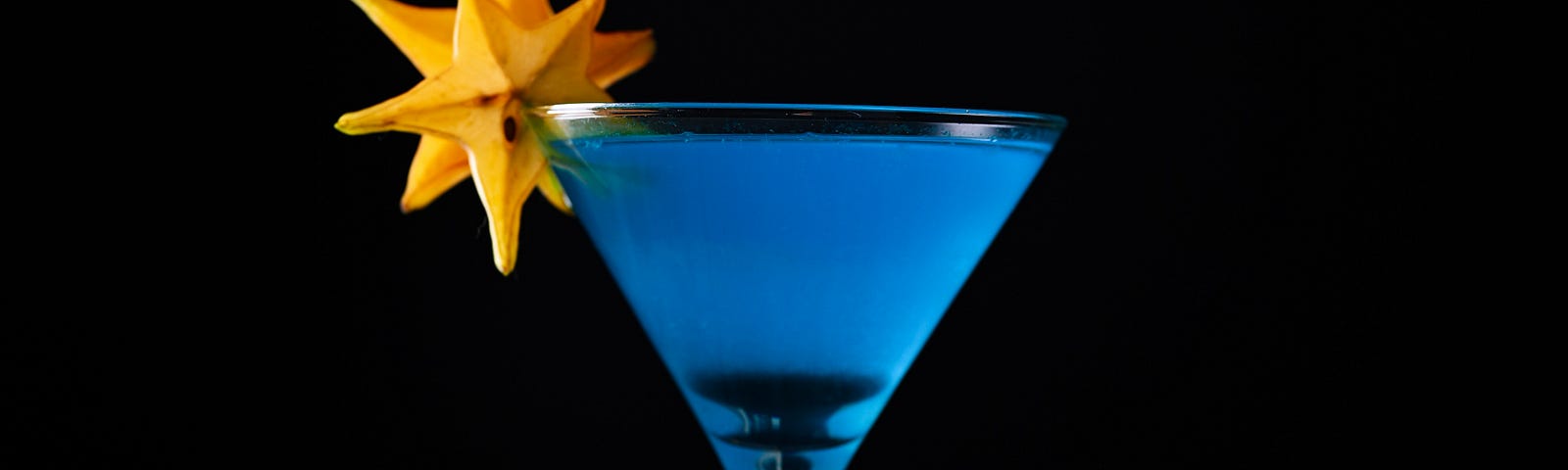 A blue cocktail is in a V-shaped glass with a stem.