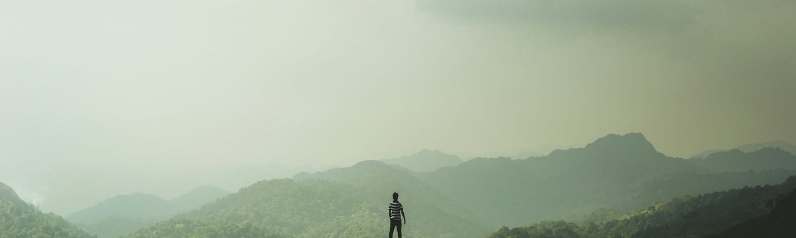 a man stands on the top of a hill among many other hills