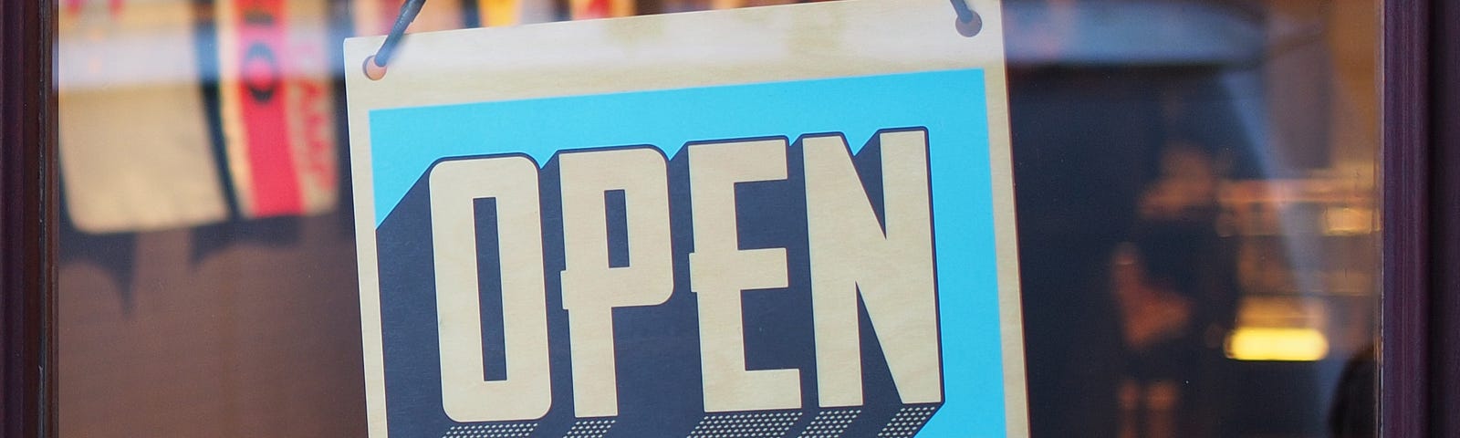 A clear glass shop door with a blue open sign hanging on it.