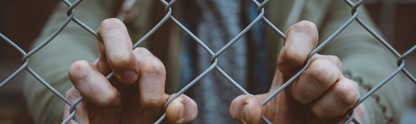 A person with their hands poking through a chain-link fence.