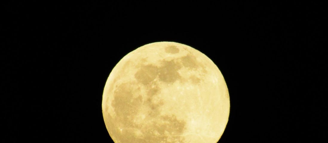 A bright, almost golden full moon in a black sky.