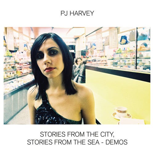 PJ Harvey “This Mess We’re In — Demo” single cover art; photo of Harvey in a black one-strap-sleeved black sequined top in a convenience store, white border with artist name on top and “STORIES FROM THE CITY, STORIES FROM THE SEA — DEMOS” text at bottom