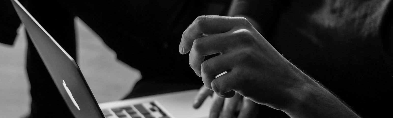 this is a photo of an apple laptop and a person is sitting in front of it. You can only see the persons hands and forearms.