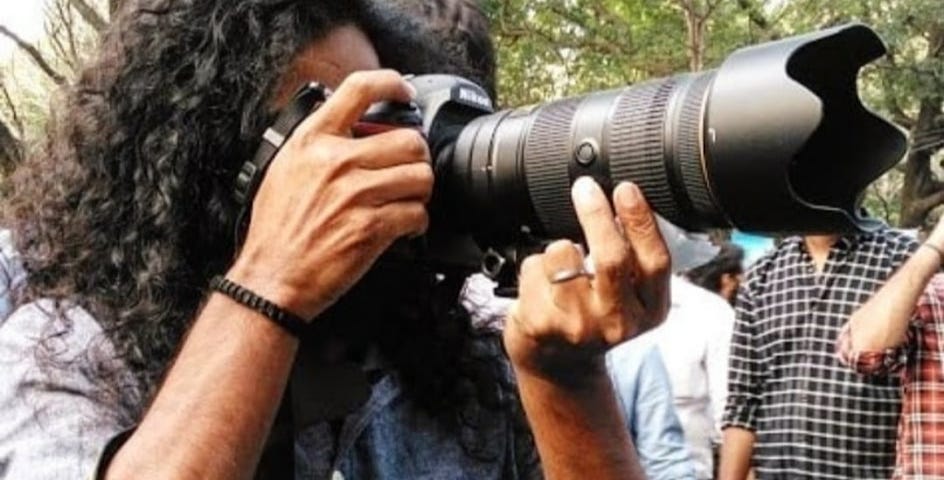 Young man in a crowd with long curly hair holding a Nikon camera with zoom lens