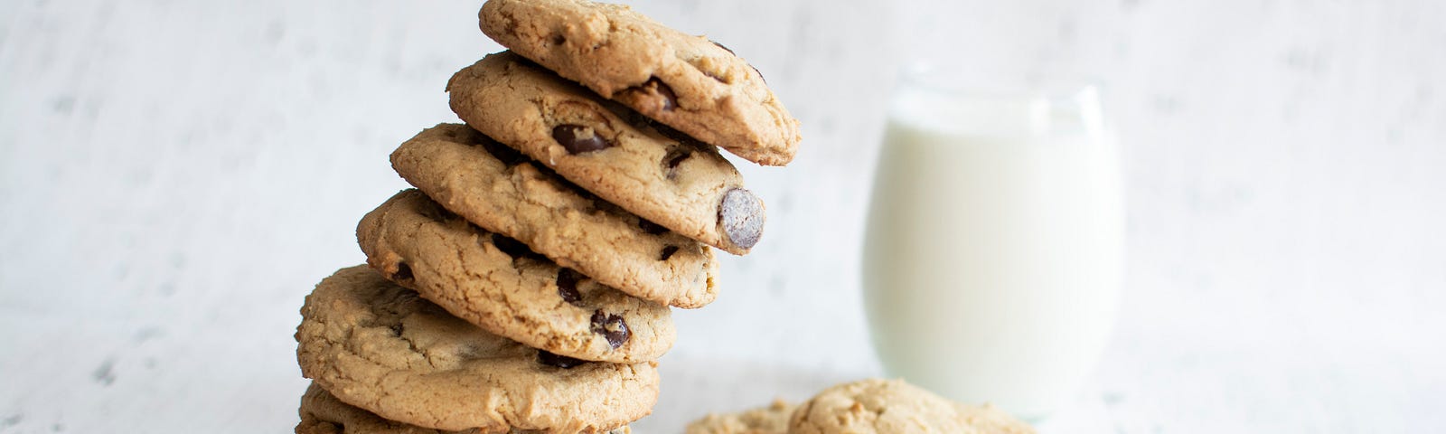 Large pile of chocolate chip cookies beside a glass of milk.