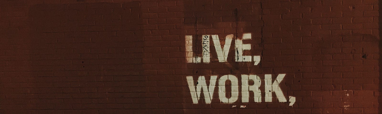 Image of a brown brick wall with the words ‘Live, Work, Create’ painted on it in white.