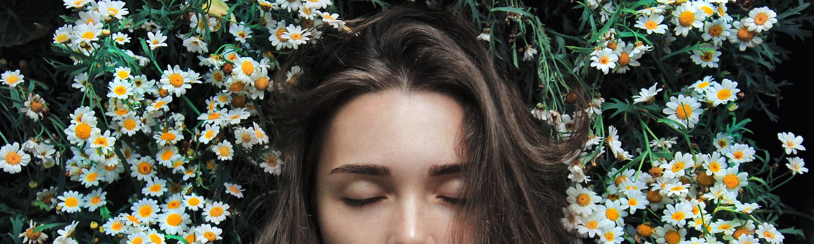 A woman’s face and shoulders, her eyes closed, lying on a bed of flowers