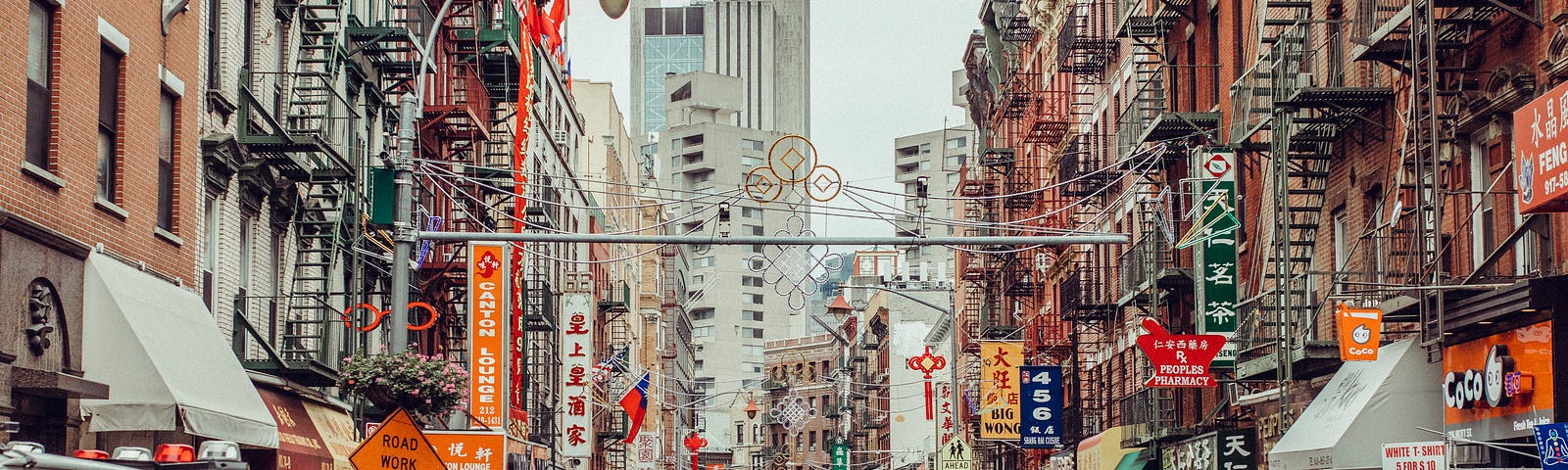 A view of Chinatown shows traffic in a narrow street, colourful banners and shop signs, people walking on crowded footpaths, and all the colour of a multi-cultural cityscape.
