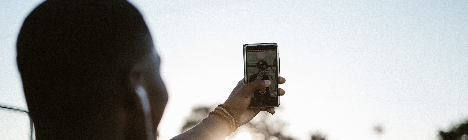 Person holding a cell phone up into a sunset.