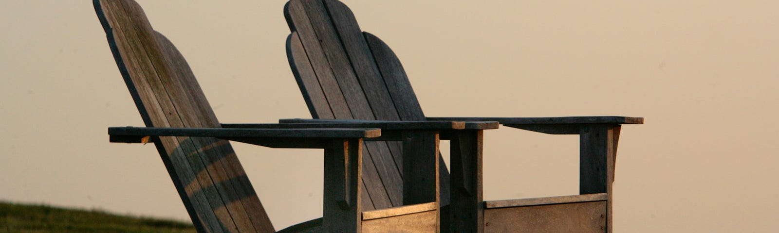 Two rustic Adirondack chairs on a lawn dimly lit by a setting sun