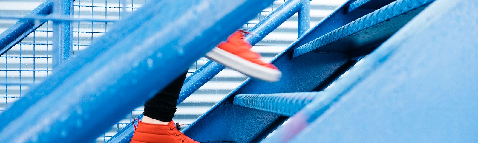 Person clad in red sneakers walks up stairs. View from side, with only shoes and legs in black clothing visible.