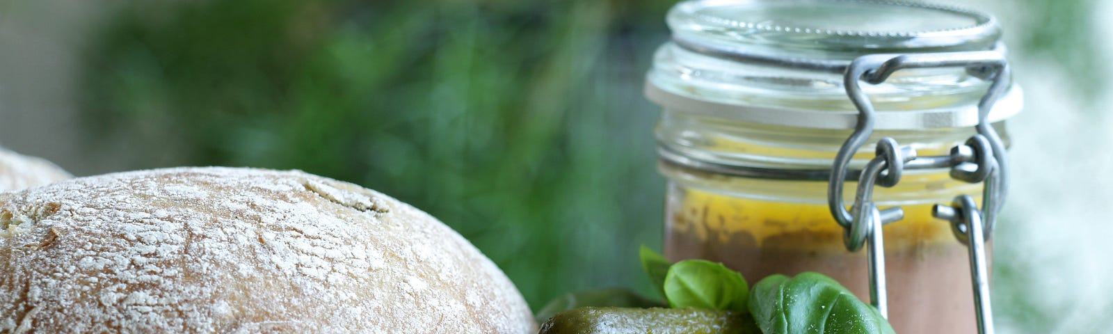 homemade bread, pickles, jar of sauce, and basil leaf on cutting board