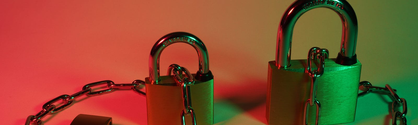 Two locked padlocks connected by a metal chain and a third unlocked padlock.
