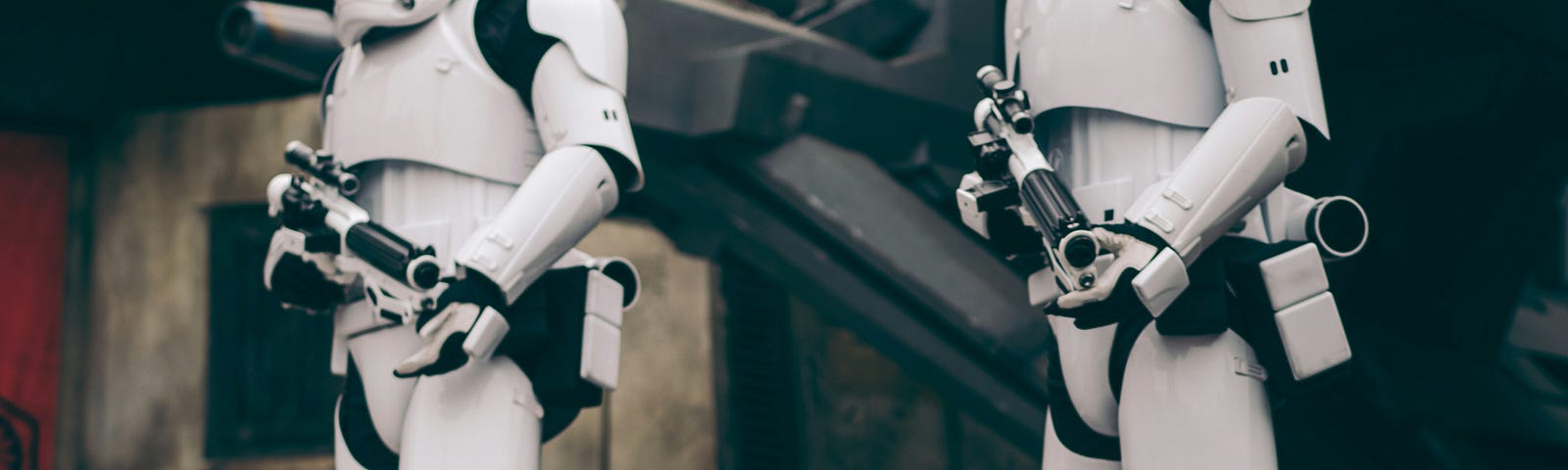 two storm troopers from the movie Star Wars, wearing their classic white space suits with black laser guns. They seem to be standing on a space ship balcony that has landed on the ground.