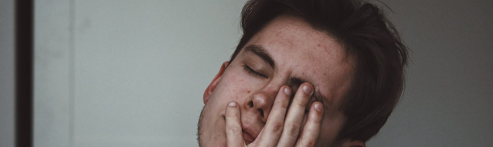 Image of a young man, eyes closed and hand held to face, deep in thought