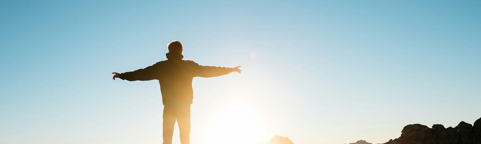 This image depicts a man with arms wide open, embracing the sunrise.