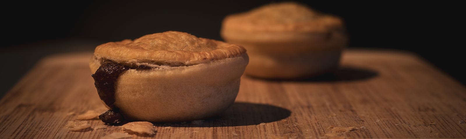 Two meat pies on a cutting board, oozing black filling