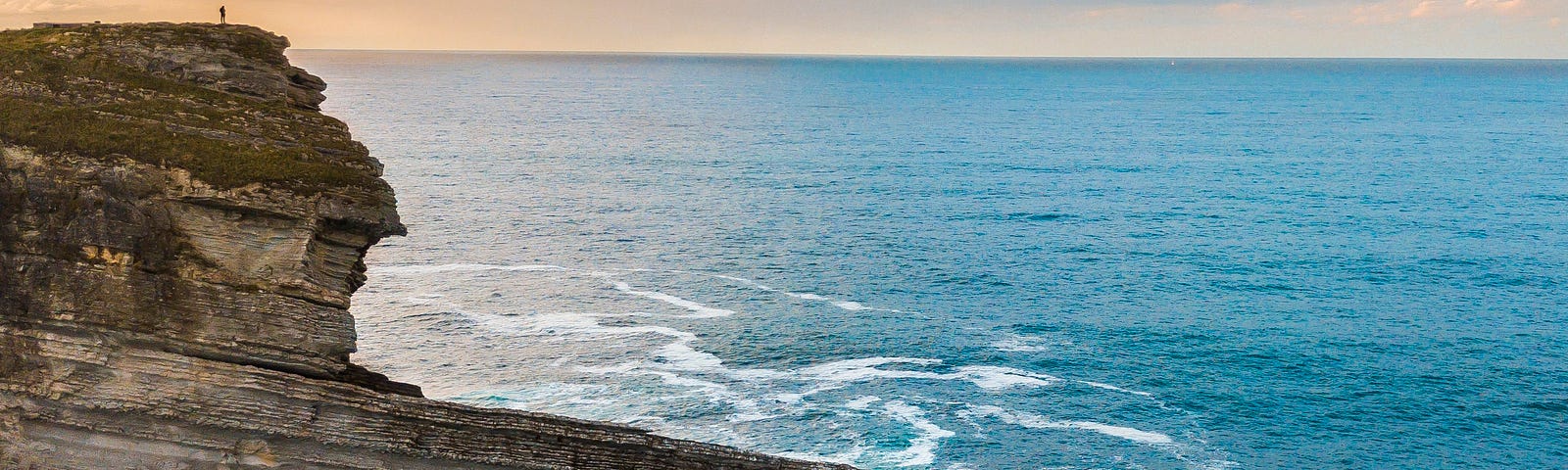 A person standing on a high cliff looking out over the ocean