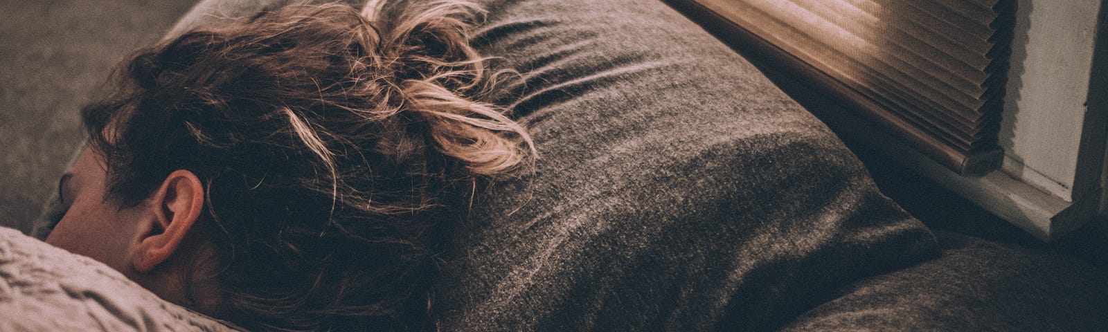 The top section of a bed, with a lady’s head lying on the pillow.