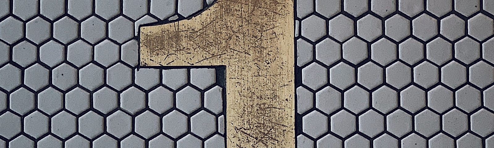 A huge metal numeral ‘one’ overlaid onto hexagonal greyish-lavender tile, alluding to the one question word in this article.