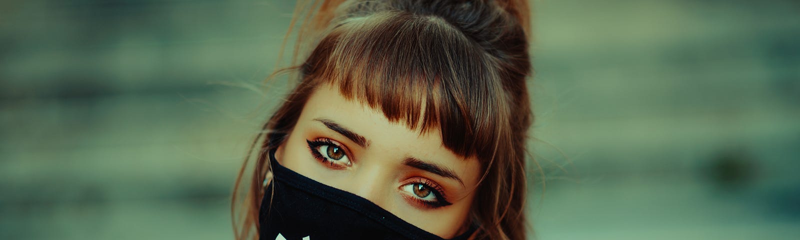 A woman with a bob hair cut and short fringe, wearing a black mask, gazes with contempt, her head tilted to the side.