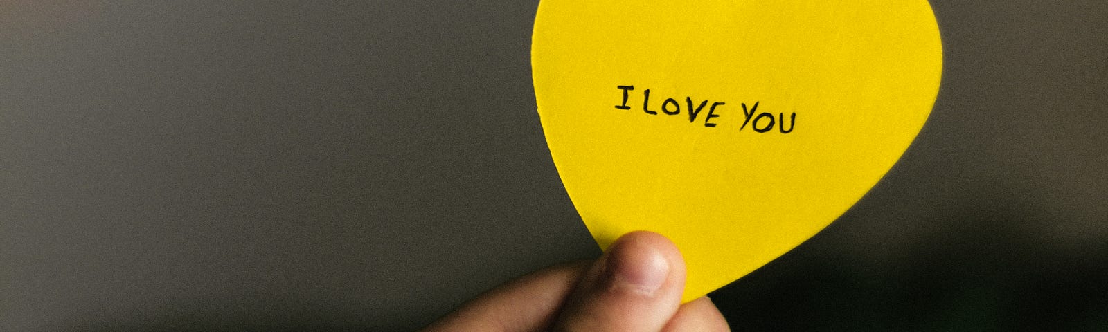 a hand holding the base of a pale pink heart-shaped paper with the words, in black and capitalised: I love you.