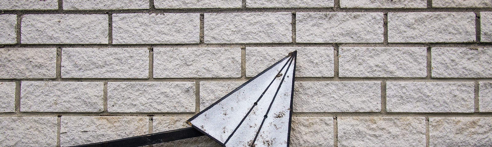A dirty white paper airplane leaning against a white brick wall