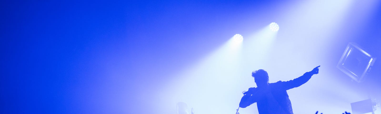 Male singer in silhouette on stage in front of large concert crowd