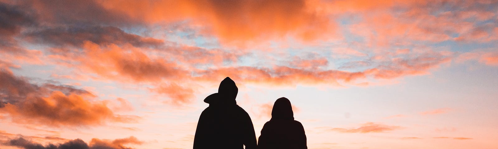 A couple holding hands outside watching the sunset.