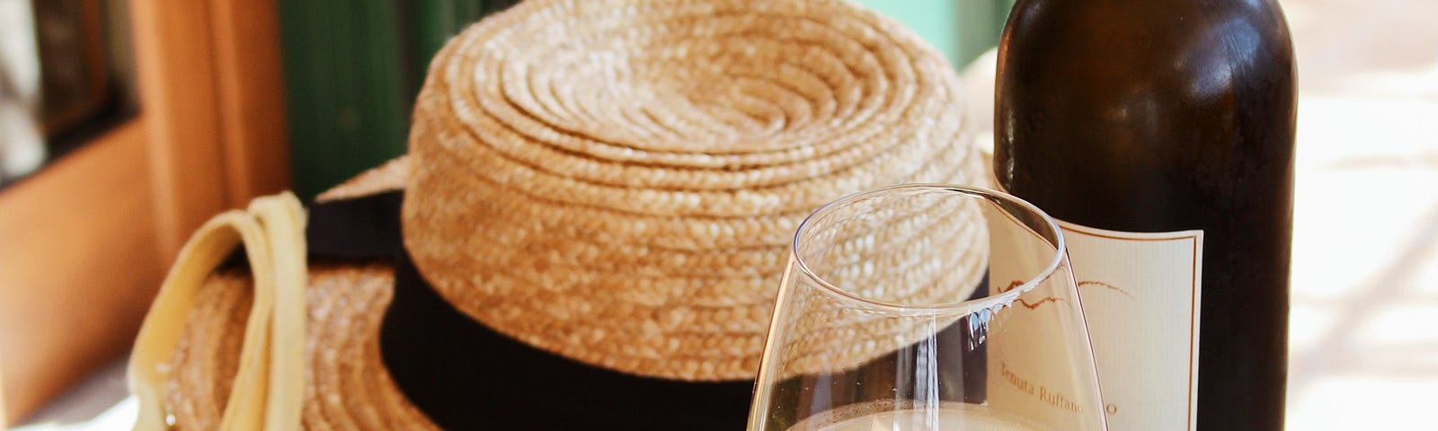 Picture of grapes, flowers, wine, and a hat set on table.