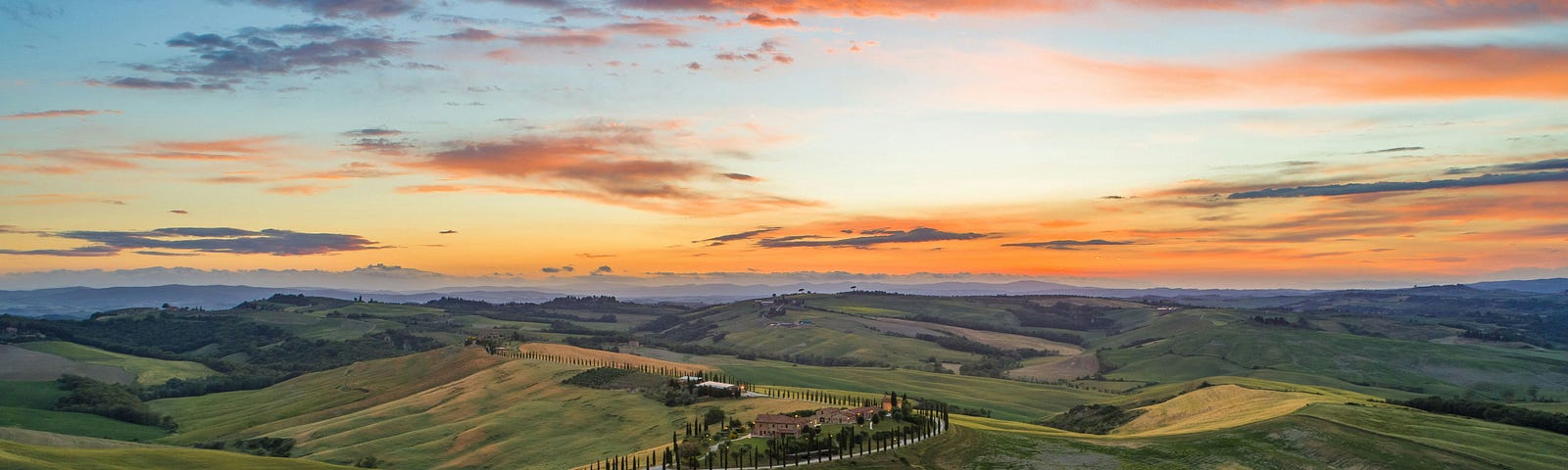 A winding road through green, hilly plains at sunrise